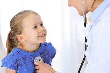 Doktor steteskopla küçük bir kızı muayene ediyor. Her zamanki tıbbi muayenede gülümseyen çocuk hasta. Tıp ve sağlık hizmetleri kavramları