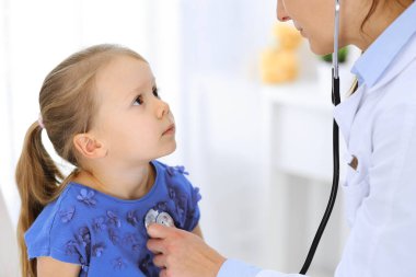 Doktor steteskopla küçük bir kızı muayene ediyor. Her zamanki tıbbi muayenede gülümseyen çocuk hasta. Tıp ve sağlık hizmetleri kavramları