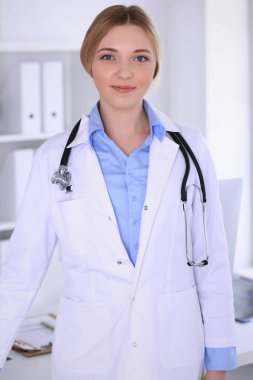 Hastanedeki genç kadın doktor kameraya bakıyor. Mavi renkli terapist bluzu iyi görünüyor. Tıp ve sağlık hizmetleri kavramı