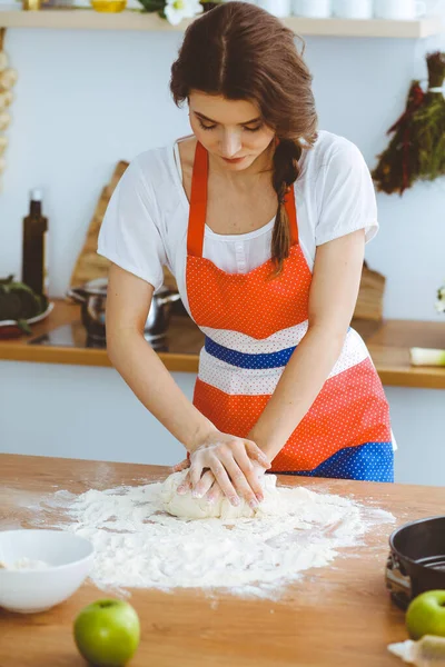 Jovem morena cozinhando pizza ou massa artesanal na cozinha. Dona de casa que prepara a massa de farinha na mesa de madeira. Conceito de alimentação, alimentação e saúde — Fotografia de Stock