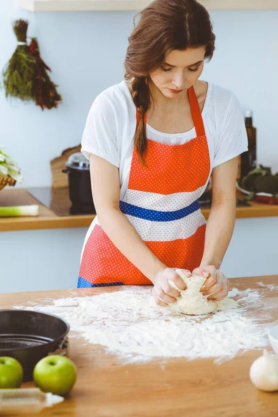 Jovem morena cozinhando pizza ou massa artesanal na cozinha. Dona de casa que prepara a massa de farinha na mesa de madeira. Conceito de alimentação, alimentação e saúde — Fotografia de Stock