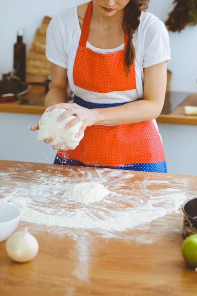 Jovem morena cozinhando pizza ou massa artesanal na cozinha. Dona de casa que prepara a massa de farinha na mesa de madeira. Conceito de alimentação, alimentação e saúde — Fotografia de Stock