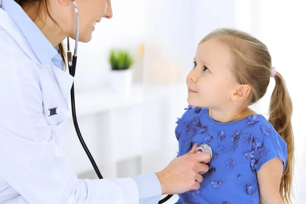 Arzt untersucht ein kleines Mädchen per Stethoskop. Glücklich lächelnder Kinderpatient bei der üblichen ärztlichen Untersuchung. Medizin- und Gesundheitskonzepte — Stockfoto