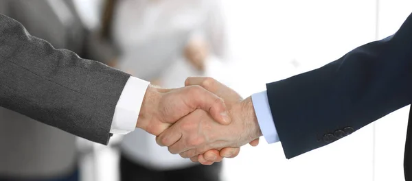 Business people shaking hands while standing with colleagues after meeting or negotiation, close-up. Group of unknown businessmen and women in modern office. Teamwork, partnership and handshake — Stock Photo, Image