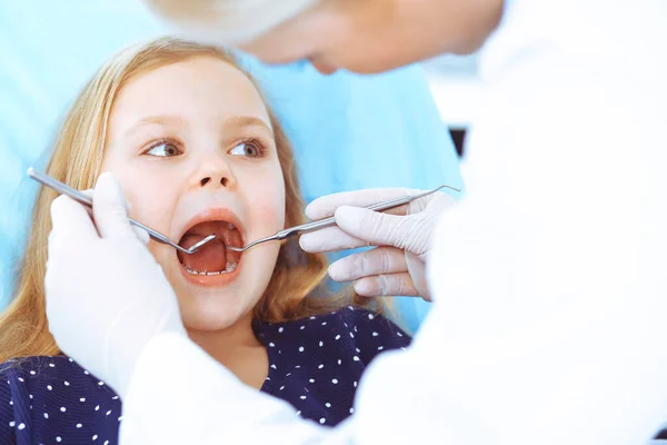 Kleines Mädchen, das mit offenem Mund am Zahnarztstuhl sitzt, während der mündlichen Untersuchung während des Arztes. Zahnarztbesuche. Medizinkonzept. Getöntes Foto — Stockfoto