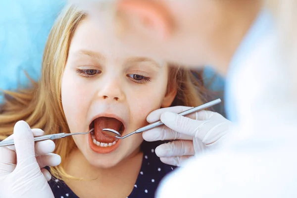 Mała dziewczynka siedzi na krześle dentystycznym z otwartymi ustami podczas kontroli doustnej, podczas gdy lekarz. Odwiedzam gabinet dentystyczny. Koncepcja medyczna. Uszkodzone zdjęcie — Zdjęcie stockowe