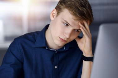 Genç sarışın iş adamı, karanlık bir ofiste iş yerinde stres hissediyor ve arka planda ışık parlıyor. Girişim işi çok çalışmak ve zamanın dışına çıkmak demektir.