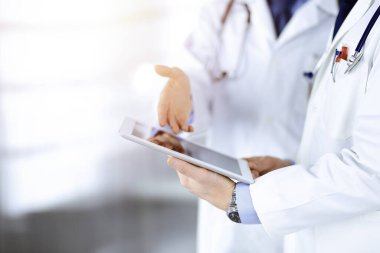 Steteskoplu kimliği belirsiz iki doktor muayene sonuçlarını tartışıyorlar, güneşli hastane ofisinde duruyorlar. Doktorlar ilaç kayıtlarını doldurmak için bir bilgisayar tableti kullanıyorlar. Mükemmel sağlık.
