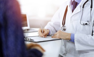 Bir doktor, hastanedeki güneşli dolapta birlikte otururken hastası için tıbbi bir reçete yazıyor. Doktor ilaç geçmişi kayıtlarını doldurmak için pano kullanıyor