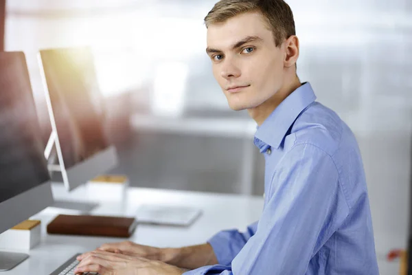 Jonge succesvolle zakenman werkt met computer, zittend aan het bureau in een zonnig modern kantoor. Hoofdfoto van een mannelijke ondernemer of IT-specialist op de werkplek. Bedrijfsconcept — Stockfoto