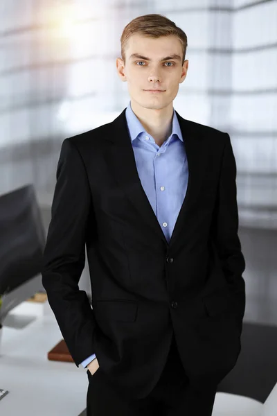 Joven hombre de negocios en un traje, mientras está de pie en una soleada oficina moderna. Éxito y concepto de trabajo empresarial —  Fotos de Stock