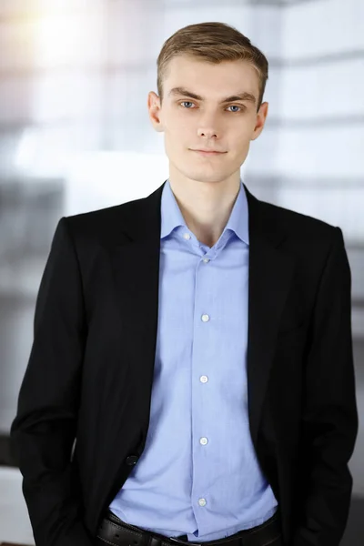 Joven hombre de negocios en un traje, mientras está de pie en una soleada oficina moderna. Éxito y concepto de trabajo empresarial —  Fotos de Stock