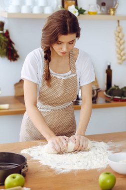 Genç esmer kadın mutfakta pizza ya da el yapımı makarna pişiriyor. Ev hanımı ahşap masada hamur hazırlıyor. Diyet, gıda ve sağlık konsepti