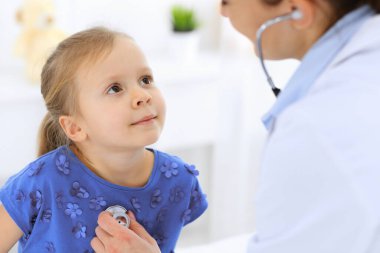 Doktor steteskopla küçük bir kızı muayene ediyor. Her zamanki tıbbi muayenede gülümseyen çocuk hasta. Tıp ve sağlık hizmetleri kavramları