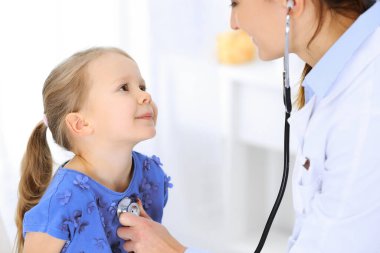 Doktor steteskopla küçük bir kızı muayene ediyor. Her zamanki tıbbi muayenede gülümseyen çocuk hasta. Tıp ve sağlık hizmetleri kavramları