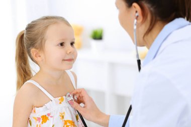 Doktor steteskopla küçük bir kızı muayene ediyor. Her zamanki tıbbi muayenede gülümseyen çocuk hasta. Tıp ve sağlık hizmetleri kavramları