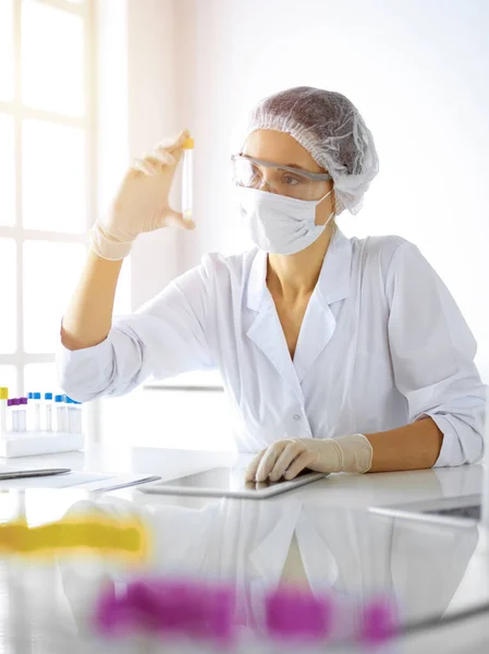 Científica profesional en gafas protectoras investigando tubo con reactivos en laboratorio soleado. Medicina e investigación — Foto de Stock