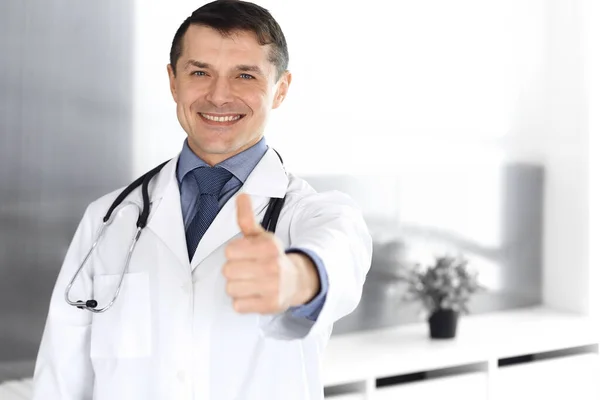 医者の男はカメラで明るい笑顔、親指を上げる。診療所での完璧な医療サービス。医学と医療における幸せな未来 — ストック写真