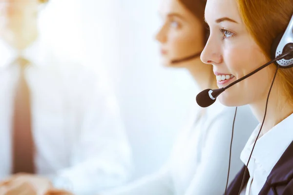 Group of diverse phone operators at work in sunny office. Handsome business woman with headphones consulting clients. Call center and business people concept — Stock Photo, Image