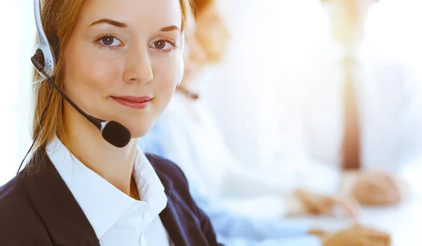 Groep van diverse telefoonoperatoren aan het werk in zonnig kantoor. Knappe zakenvrouw met een koptelefoon die klanten raadpleegt. Call center en business people concept Stockfoto