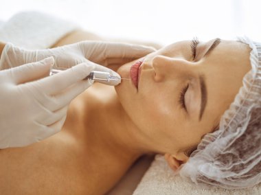 Güzellik uzmanı, genç esmer kadının yüzüne şırıngayla güzellik prosedürü uyguluyor. Kozmetik ilaç ve ameliyat, güzellik iğneleri.