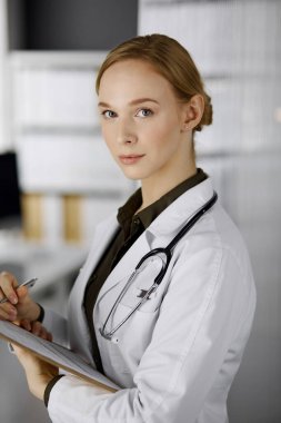 Klinikte pano kullanan neşeli gülümseyen kadın doktor. İş yerindeki dost canlısı doktor kadın portresi. Hastanede mükemmel bir tıbbi hizmet. Tıp konsepti