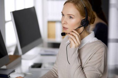 İş kadını ofiste otururken kulaklıkla konuşuyor. Çağrı merkezi ve çeşitli iş grupları
