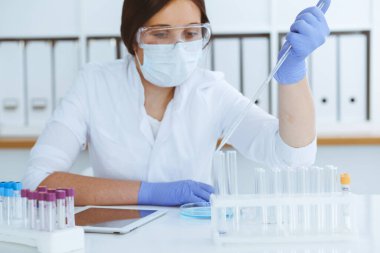 Koruyucu gözlüklü profesyonel kadın bilim adamının laboratuarda reaktörlerle deney yapması. Tıp ve araştırma konsepti