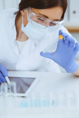 Koruyucu gözlüklü profesyonel kadın bilim adamının laboratuarda reaktörlerle deney yapması. Tıp ve araştırma konsepti