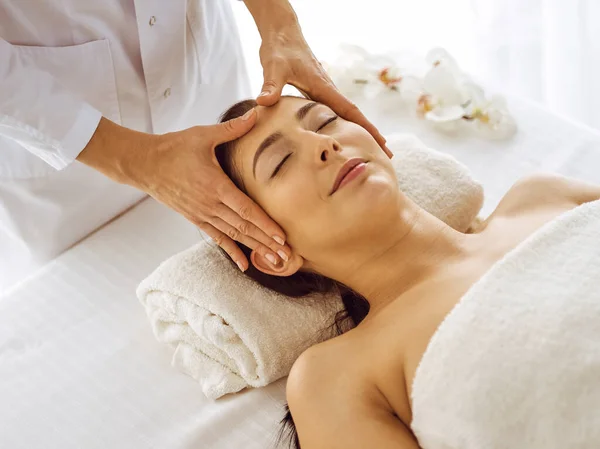 Bella donna bruna che gode di un massaggio facciale con gli occhi chiusi. Rilassante trattamento in medicina e spa concetti di centro — Foto Stock
