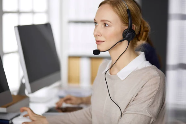 Femme d'affaires parlant par casque pendant qu'elle était assise au bureau. Centre d'appels et divers groupes de personnes en affaires — Photo