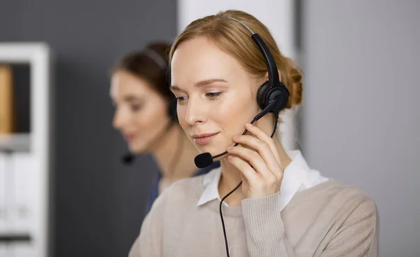 Üzletasszony fülhallgatóval beszél, miközben az irodában ül. Call center és változatos emberek csoport az üzleti életben — Stock Fotó