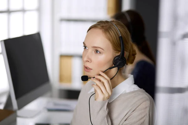 Femme d'affaires parlant par casque pendant qu'elle était assise au bureau. Centre d'appels et divers groupes de personnes en affaires — Photo