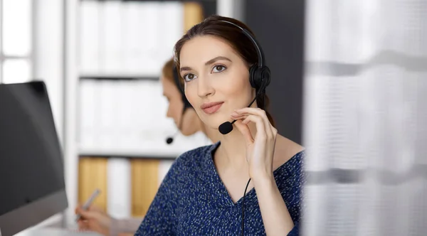 Empresaria latinoamericana hablando por auriculares mientras está sentada en el cargo. Centro de llamadas y grupo de personas diversas en los negocios —  Fotos de Stock