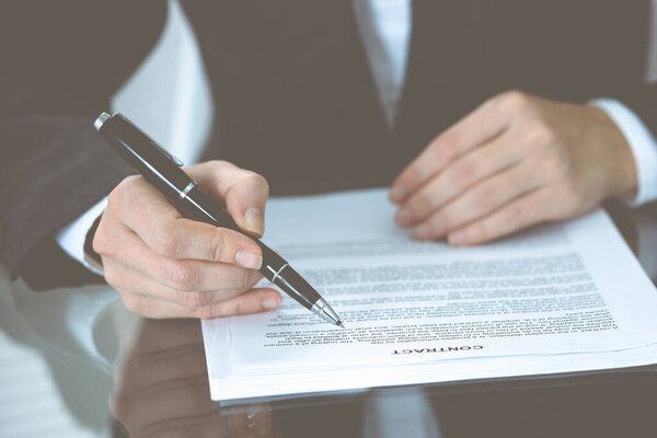 Unknown female hands with pen over document of contract. Agreement signing or business concept