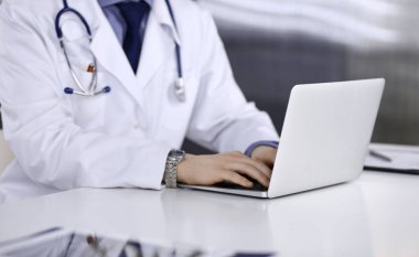 Bilinmeyen bir erkek doktor klinikte dizüstü bilgisayarla yakın planda çalışıyor. İşteki genç doktor. Mükemmel sağlık hizmeti, tıp konsepti