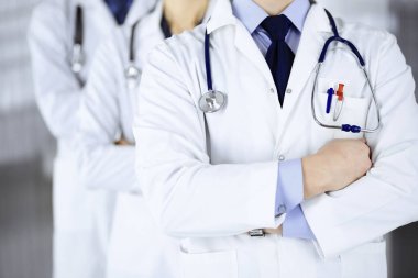 Hastane ofisinde çapraz kolları ve steteskopları olan bir grup modern doktor bir takım gibi duruyor. Doktorlar hastaları muayene etmeye ve yardım etmeye hazır. Tıbbi yardım, sağlık sigortası, en iyi hastalık