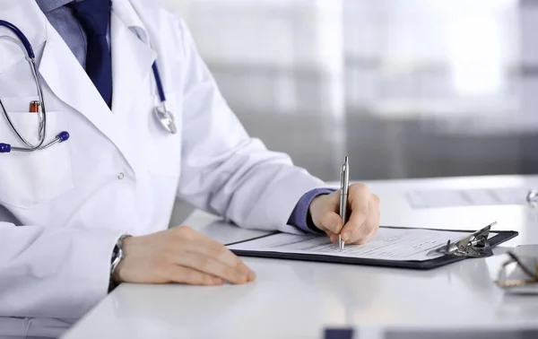 Médico desconhecido sentado e trabalhando com prancheta de registro de histórico de medicação na clínica em seu local de trabalho, close-up. Médico jovem no trabalho. Serviço médico perfeito, conceito de medicina — Fotografia de Stock