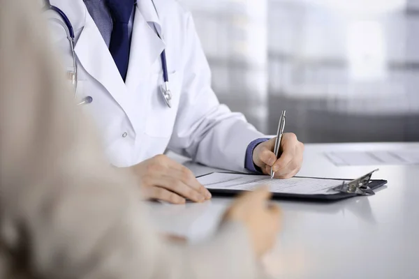 Médico desconhecido e mulher paciente discutindo algo enquanto estava sentado na clínica e usando prancheta. Melhor serviço médico no hospital, medicina, parada pandêmica — Fotografia de Stock