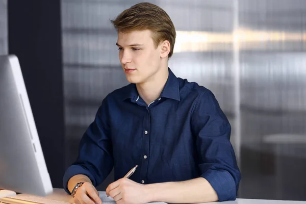 Jeune homme d'affaires blond réfléchissant à la stratégie à son lieu de travail avec ordinateur. Démarrage d'entreprise signifie travailler dur et hors du temps pour la réussite — Photo
