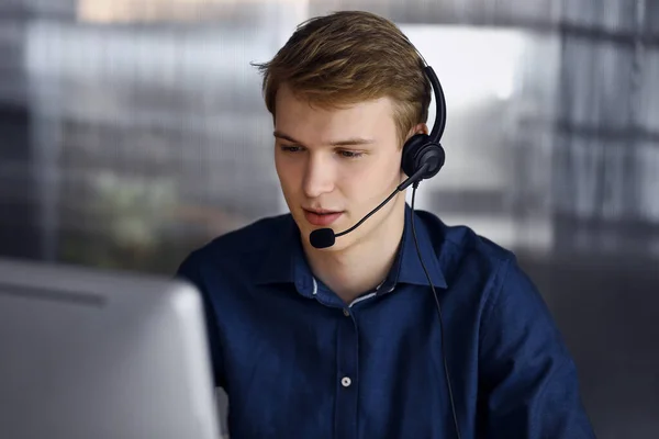 Young blond businessman using headset and computer at work. Startup business means working hard and out of time for success achievement