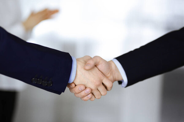 Business people shaking hands at meeting or negotiation, close-up. Group of unknown businessmen and a woman standing in a modern office. Teamwork, partnership and handshake concept