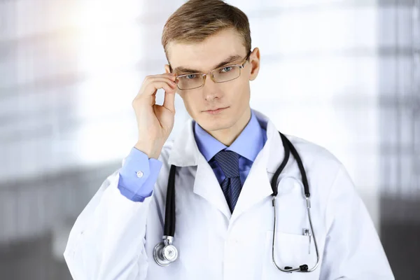 El doctor, con gafas y estetoscopio, está de pie en su soleado consultorio del hospital. Servicio médico perfecto en la clínica. Futuro feliz en medicina y salud — Foto de Stock