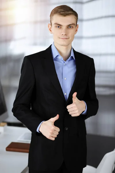 Joven hombre de negocios en un traje, mientras está de pie en una soleada oficina moderna. Éxito y concepto de trabajo empresarial — Foto de Stock