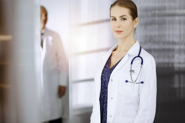 Allegro medico donna in piedi in clinica soleggiata. Ritratto di amichevole sorridente donna-medico. Concetto di medicina — Foto Stock