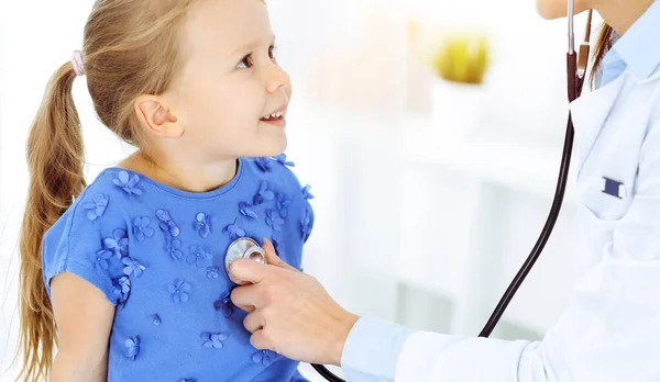 닥터가 맑은 병원에서 청진기로 아이를 진찰하고 있어. 푸른 옷을 입고 있는 행복 한 미소짓는 소녀는 언제나 병원에서 진찰을 받는다 — 스톡 사진