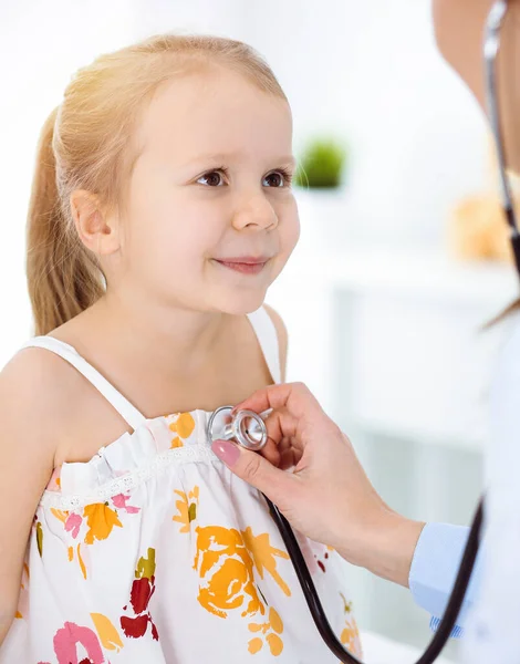 Lekarz badający dziecko stetoskopem w słonecznej klinice. Szczęśliwy uśmiech pacjenta dziewczyna ubrana w jasny kolor sukienka jest w zwykłej inspekcji medycznej — Zdjęcie stockowe