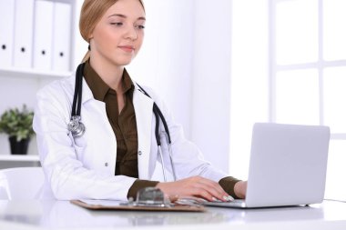 Hastanedeki genç bayan doktor bilgisayar monitörüne bakıyor. Doktor ilaç geçmişi ve sınav sonuçlarını kontrol ediyor. Tıp ve sağlık hizmetleri kavramı