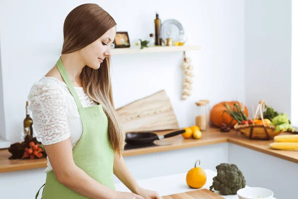 Mooie vrouw gekleed in een schort kookt eten in de keuken. Huisvrouw snijdt verse veganistische salade — Stockfoto