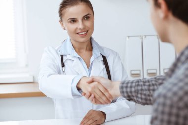 Kadın doktor, erkek hastasıyla tokalaşırken gülümsüyor. Tıp konsepti